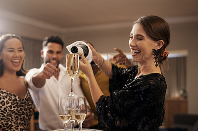 Buy stock photo Shot of an attractive young woman standing and pouring champagne for her friends during a New Year's dinner party