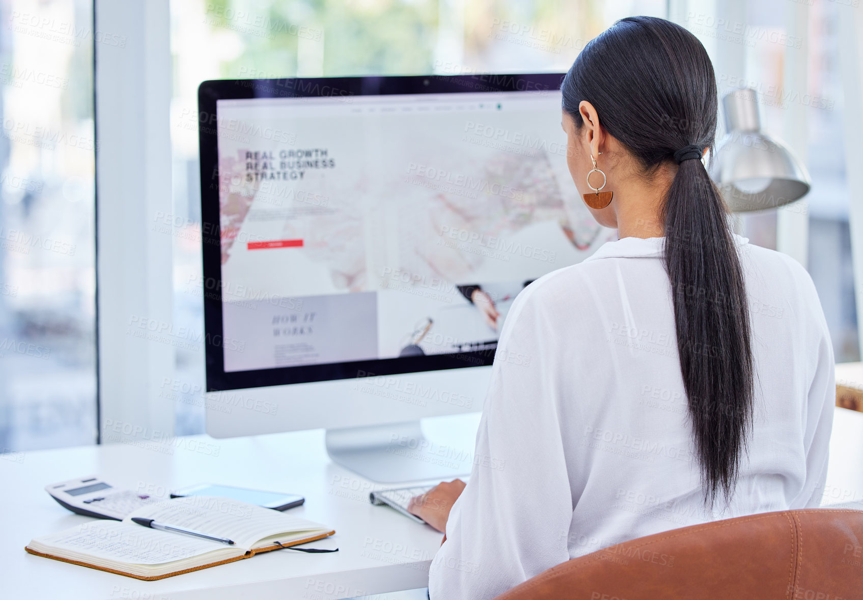 Buy stock photo Rear view shot of a young businesswoman using her laptop in a modern office