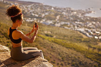 Buy stock photo Shot of a woman taking pictures with her cellphone while sitting on a mountain cliff