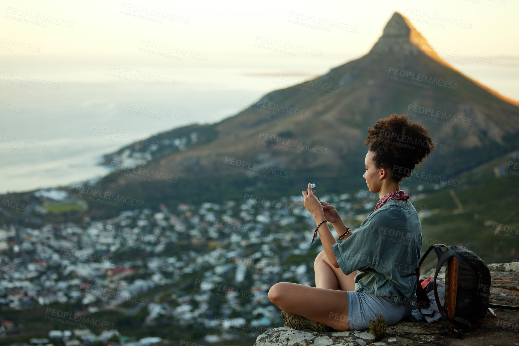 Buy stock photo Woman, hiking and phone on mountain for travel in cape town for wellness on the weekend. Female hiker, mobile and adventure on a cliff with cityscape for scenery of lion's head in the outdoor.