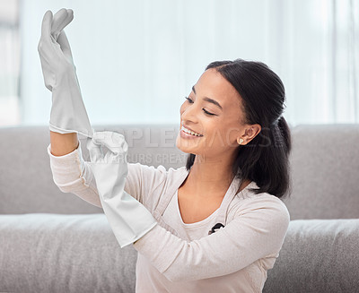 Buy stock photo Shot of a young woman putting on gloves at home