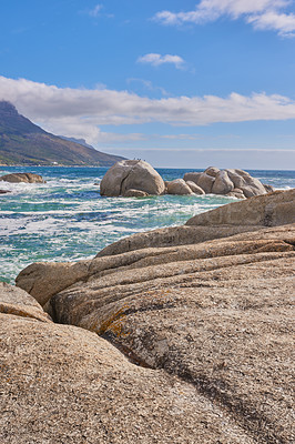 Buy stock photo Beautiful sea view of a big boulders and ocean water on a sunny beach day in summer. A seaside setting in nature with a blue sky, white clouds, and waves. A seascape near a shore and mountains.