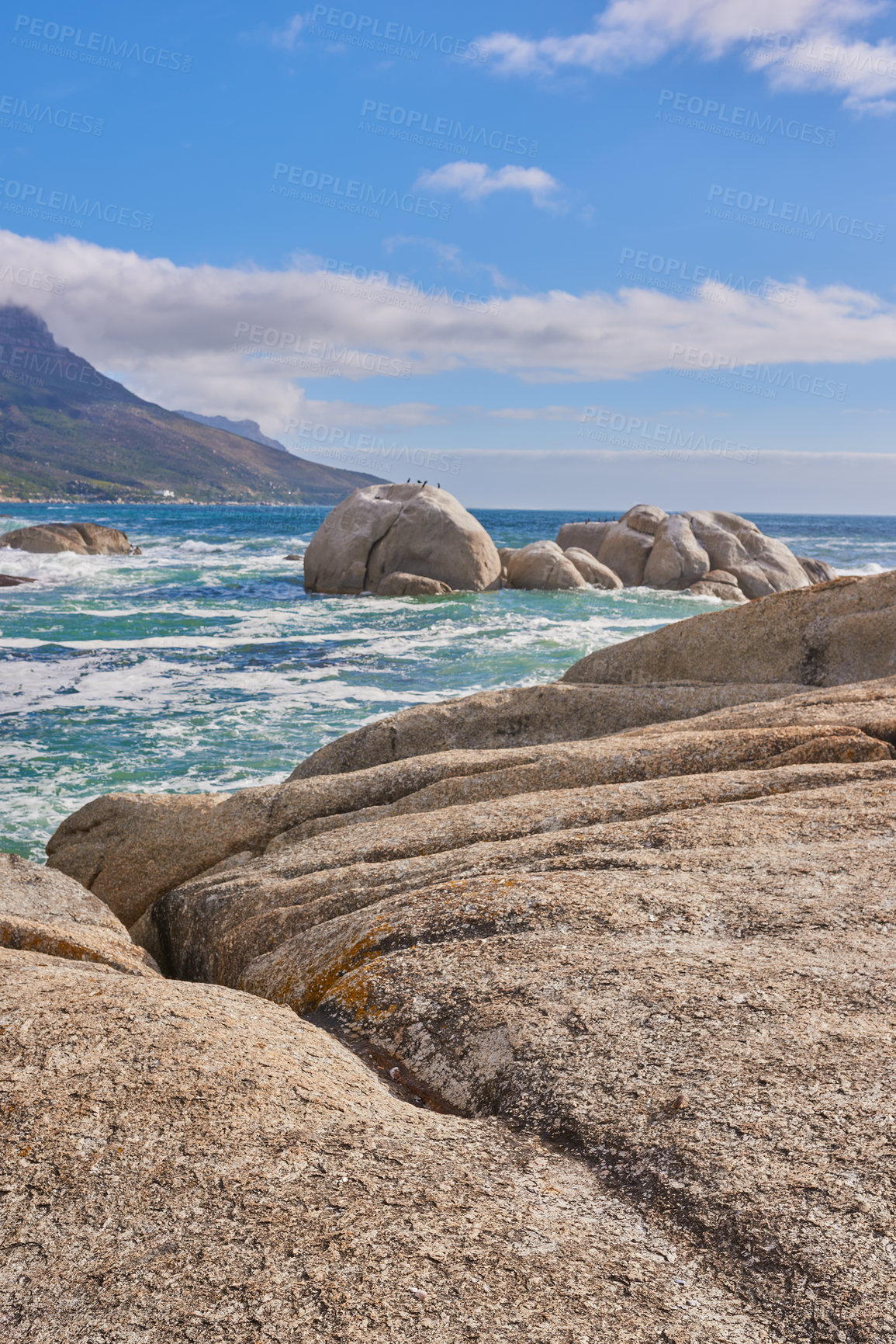 Buy stock photo Beautiful sea view of a big boulders and ocean water on a sunny beach day in summer. A seaside setting in nature with a blue sky, white clouds, and waves. A seascape near a shore and mountains.