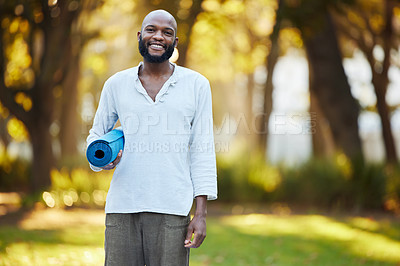 Buy stock photo Cropped portrait of a handsome young man holding his yoga mat while standing outside in the park