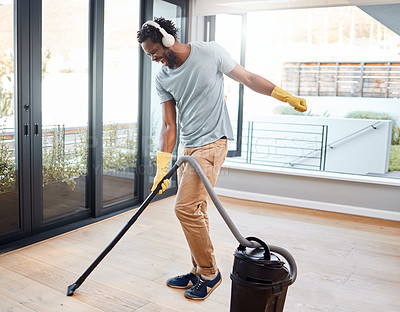 Buy stock photo Shot of a young man wearing headphones while vacuuming at home