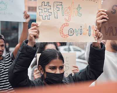 Buy stock photo Cropped shot of an attractive young woman holding up a sign protesting against the covid 19 vaccine with other demonstrators in the background