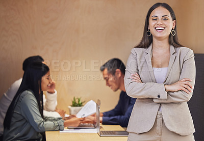 Buy stock photo Cropped portrait of an attractive young businesswoman standing with her arms crossed in the boardroom with her colleagues in the background