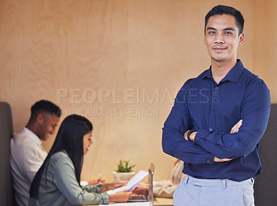 Buy stock photo Cropped portrait of a handsome young businessman standing with his arms crossed in the boardroom with his colleagues in the background