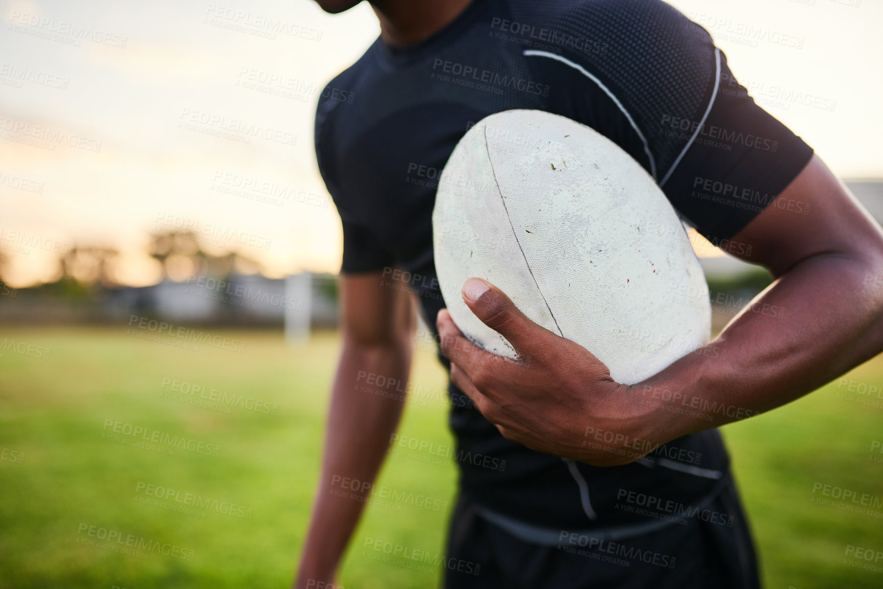 Buy stock photo Cropped shot of an unrecognizable sportsman standing alone and holding a rugby ball before an early morning practice