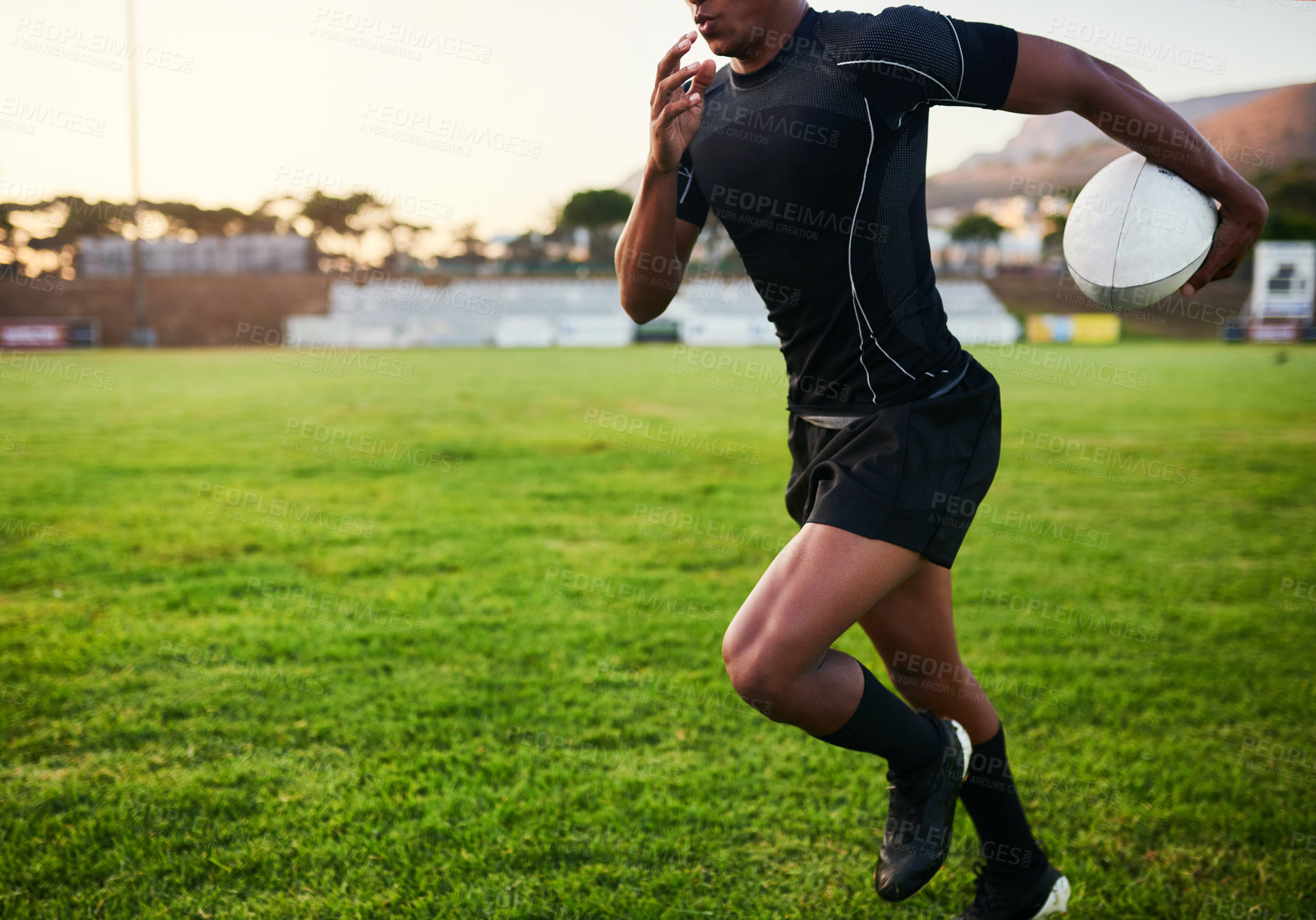 Buy stock photo Cropped shot of an unrecognizable sportsman running alone while holding a rugby ball during an early morning practice