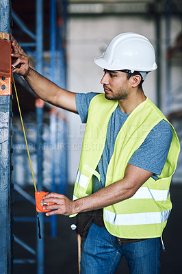 Buy stock photo Shot of a young builder using a measuring tape at a construction site