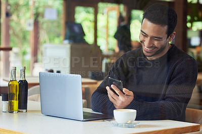 Buy stock photo Shot of a man using his cellphone while sitting with his laptop in a cafe
