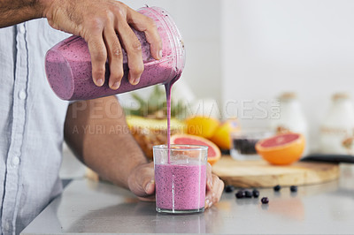 Buy stock photo Cropped shot of a man pouring a freshly blended smoothie into his glass at home
