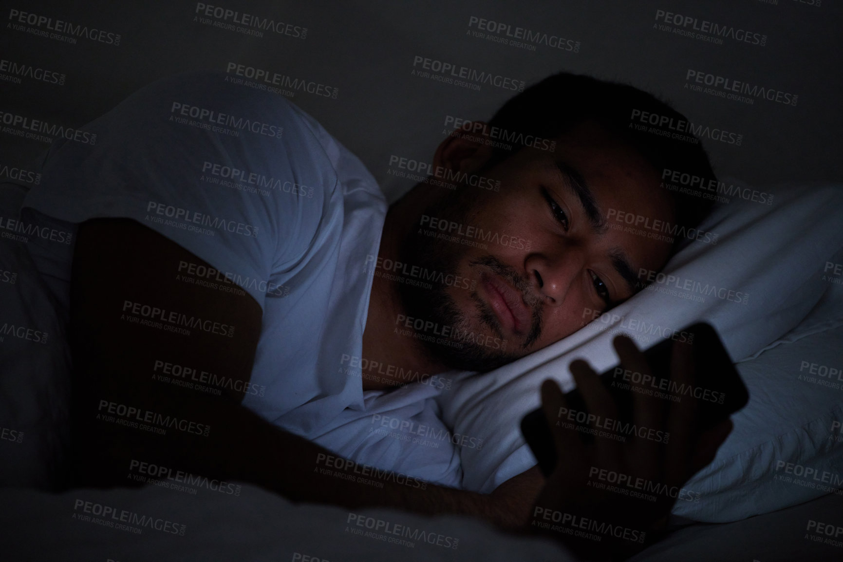 Buy stock photo Cropped shot of a man using his cellphone while lying in bed at night
