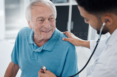 Buy stock photo Shot of a young doctor examining a mature man with a stethoscope in an office