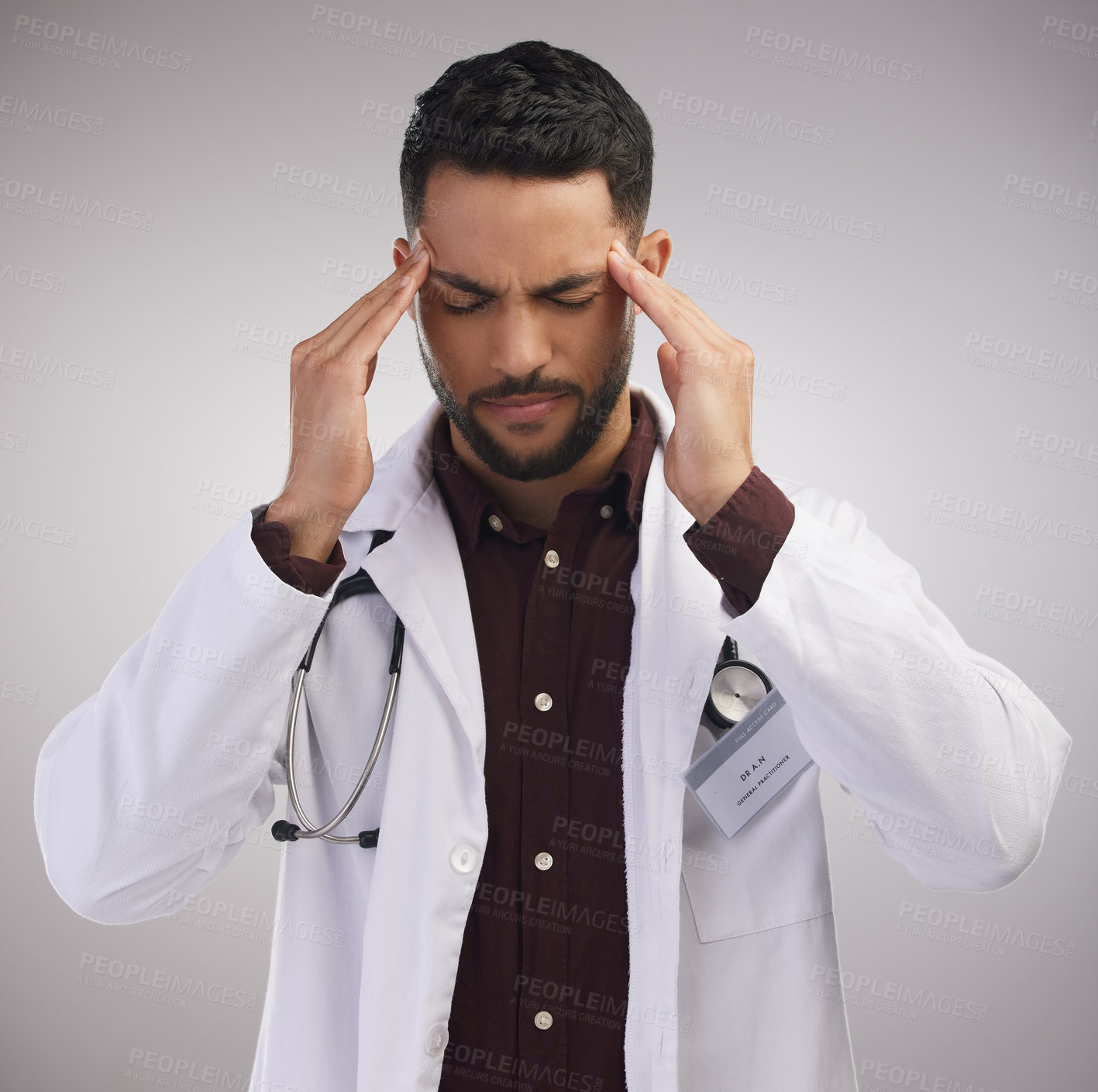 Buy stock photo Shot of a handsome young doctor standing alone in the studio and suffering from a headache
