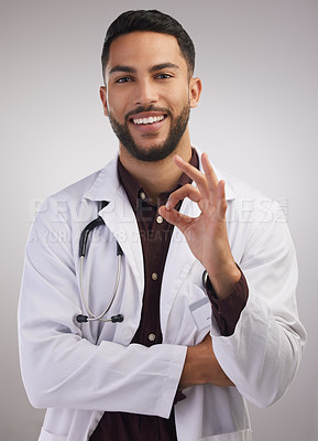 Buy stock photo Portrait, doctor and ok gesture in studio for healthcare, medical and staff in lab coat by grey background. Professional male person, stethoscope and career in clinic with pride for medicine and job