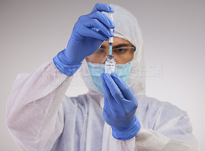 Buy stock photo Shot of a medical professional standing in a disposable hazmat suit and using a syringe to prepare a Covid vaccination