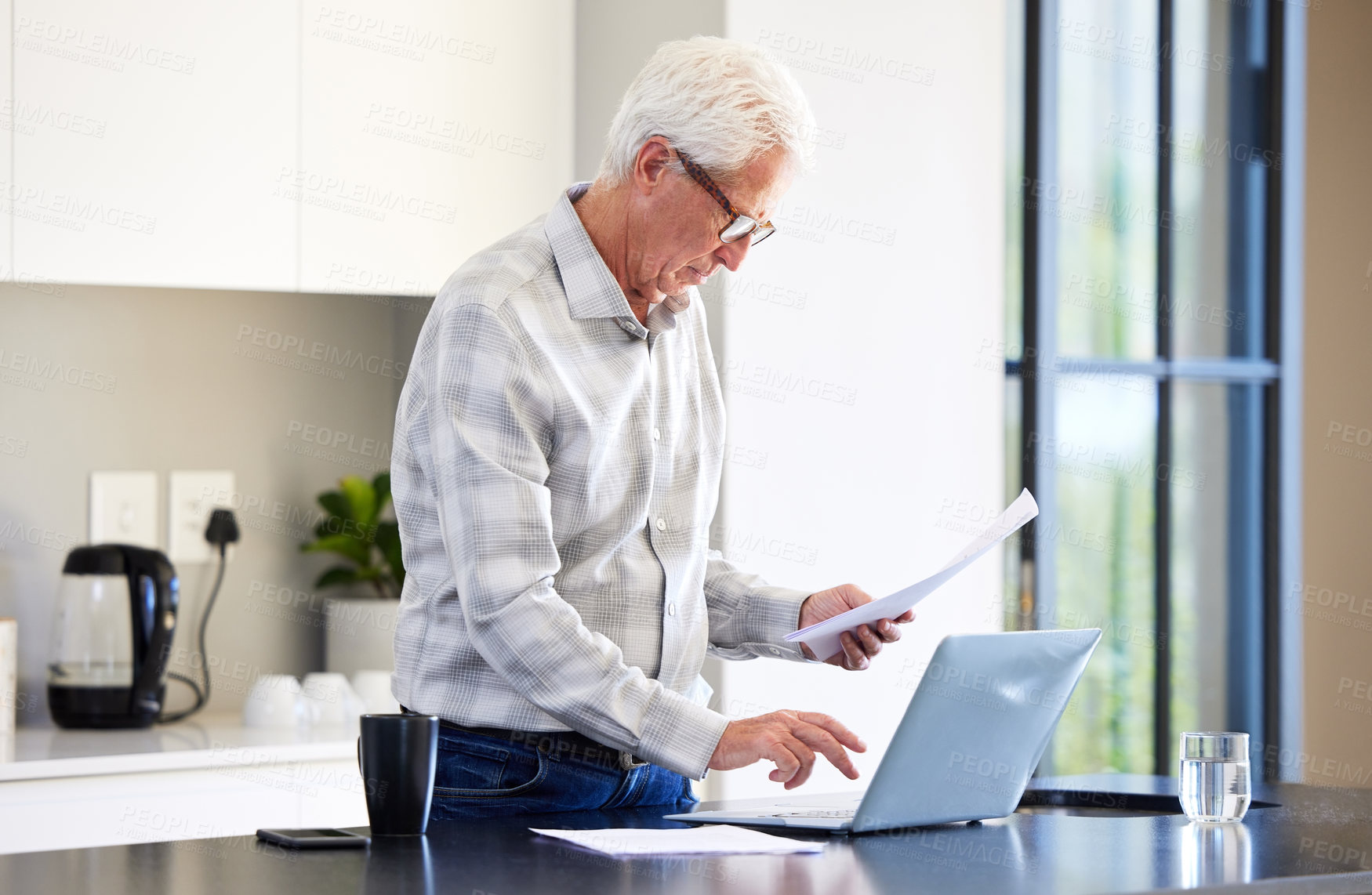 Buy stock photo Mature man, laptop and kitchen with paperwork or document for company with work from home. Report, tech and retired financial manager in house for budget or will with testament for legacy wealth.