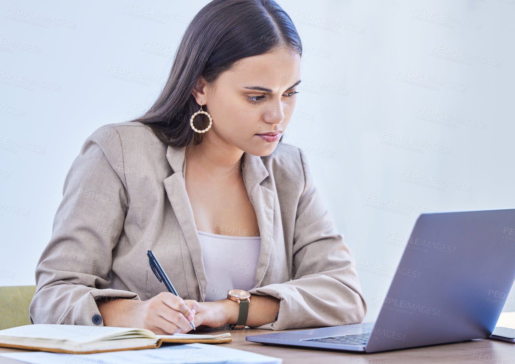 Buy stock photo Shot of a young businesswoman writing notes while working on a laptop in an office