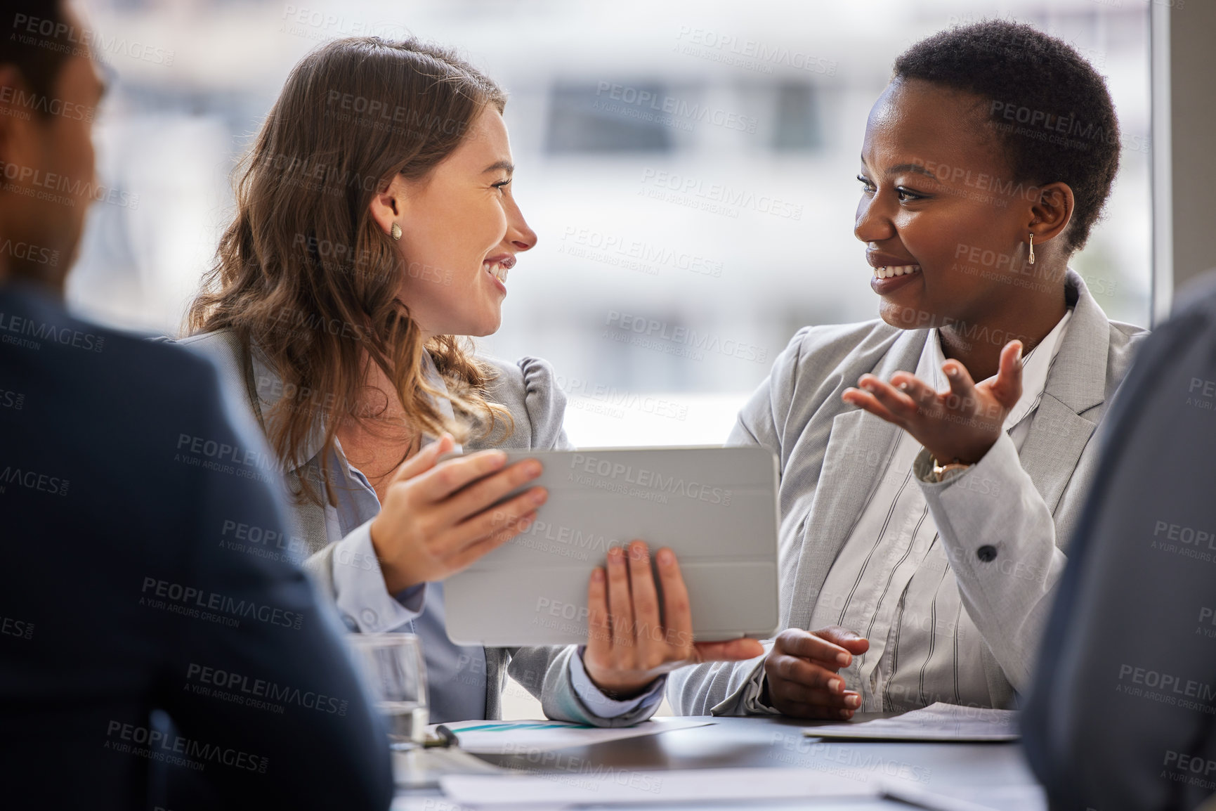 Buy stock photo Shot of two young businesswomen sitting together in the office and having a discussion while using a digital tablet
