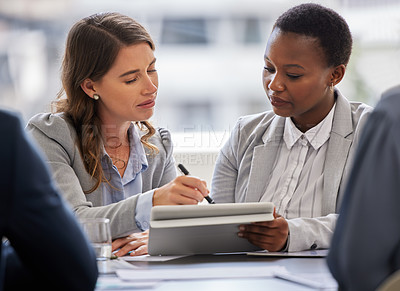 Buy stock photo Shot of two young businesswomen sitting together in the office and having a discussion while using a digital tablet