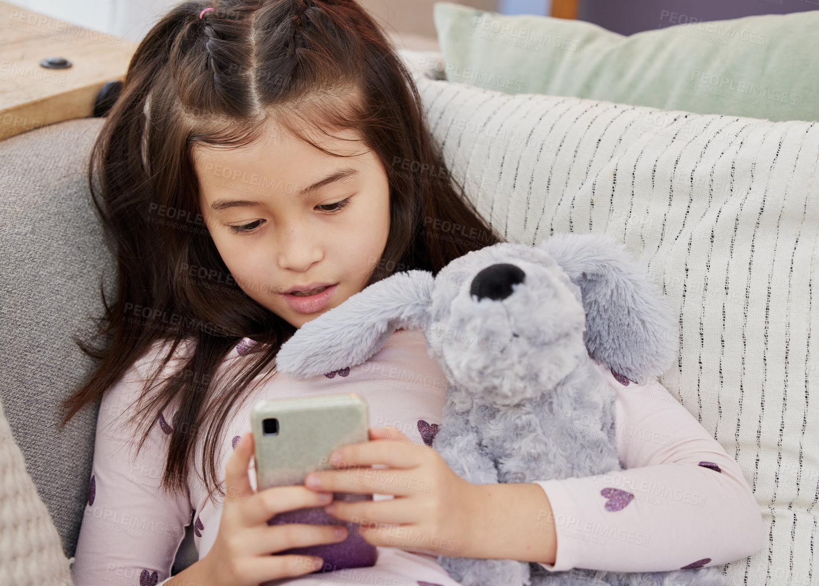 Buy stock photo Shot of a little girl using a cellphone while sitting at home with her teddybear