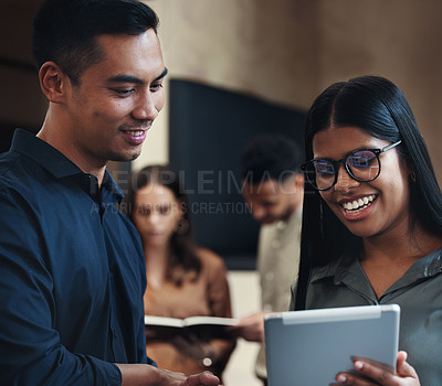 Buy stock photo Cropped shot of two young businesspeople looking over a tablet in the office with their colleagues in the background