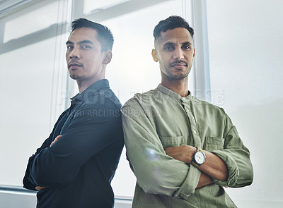 Buy stock photo Cropped portrait of two handsome young businessmen standing back to back with their arms folded in their office