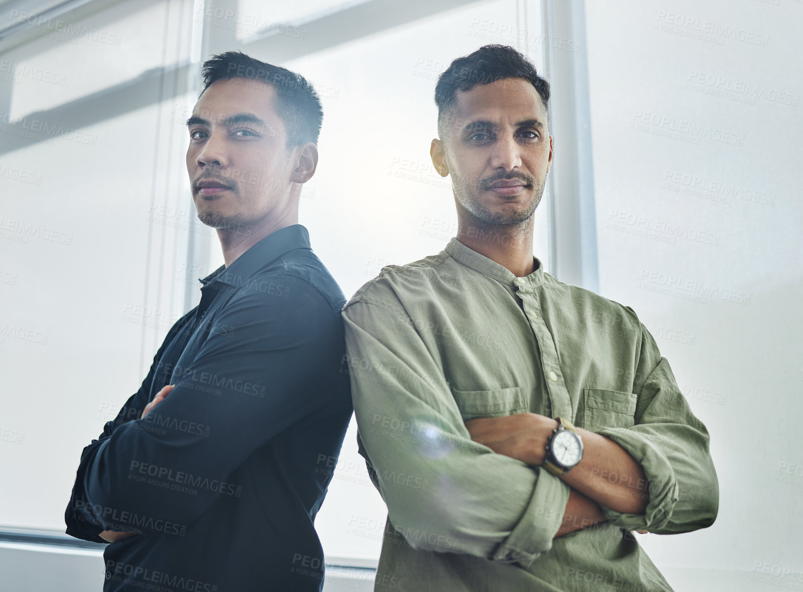 Buy stock photo Cropped portrait of two handsome young businessmen standing back to back with their arms folded in their office
