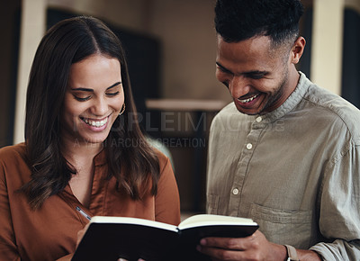 Buy stock photo Cropped shot of two young businesspeople looking over a notebook together in their office