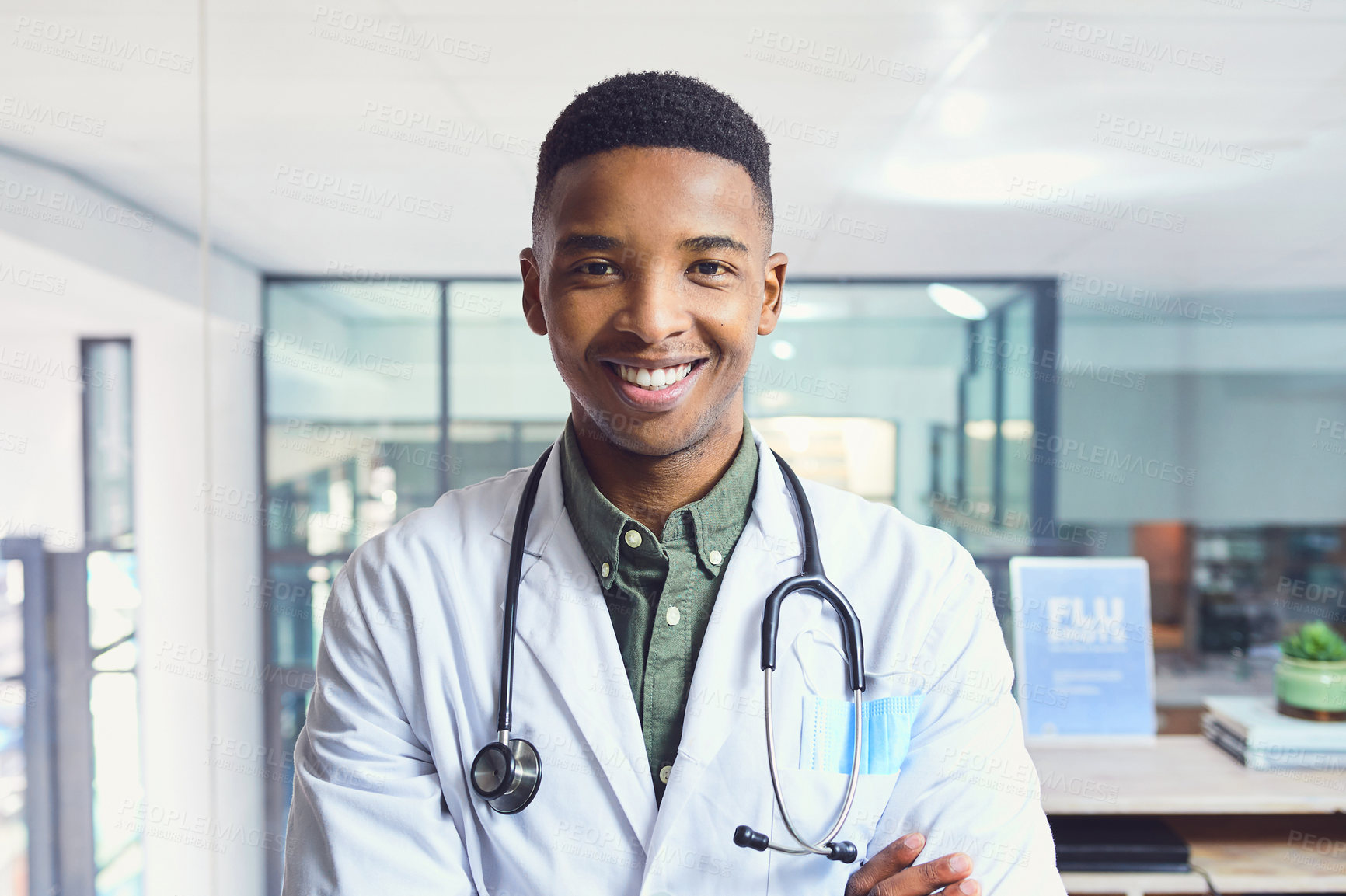 Buy stock photo Cropped portrait of a handsome young male doctor standing with his arms folded in the hospital