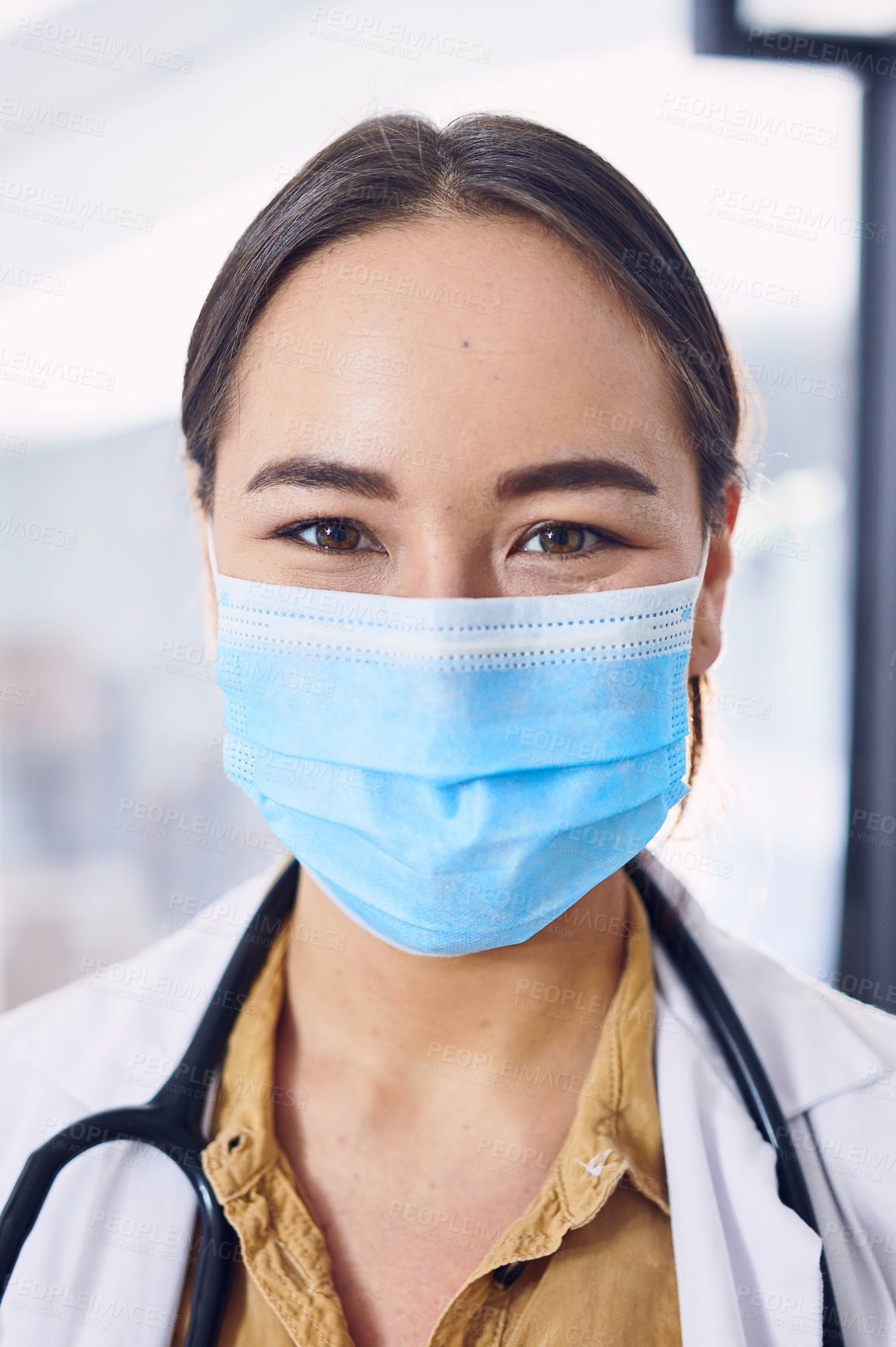 Buy stock photo Cropped portrait of an attractive young female doctor wearing a mask while standing in the hospital