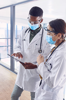 Buy stock photo Cropped shot of two young doctors working on a digital tablet while standing in the hospital
