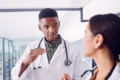 Buy stock photo Cropped shot of two young doctors discussing working while standing in the hospital
