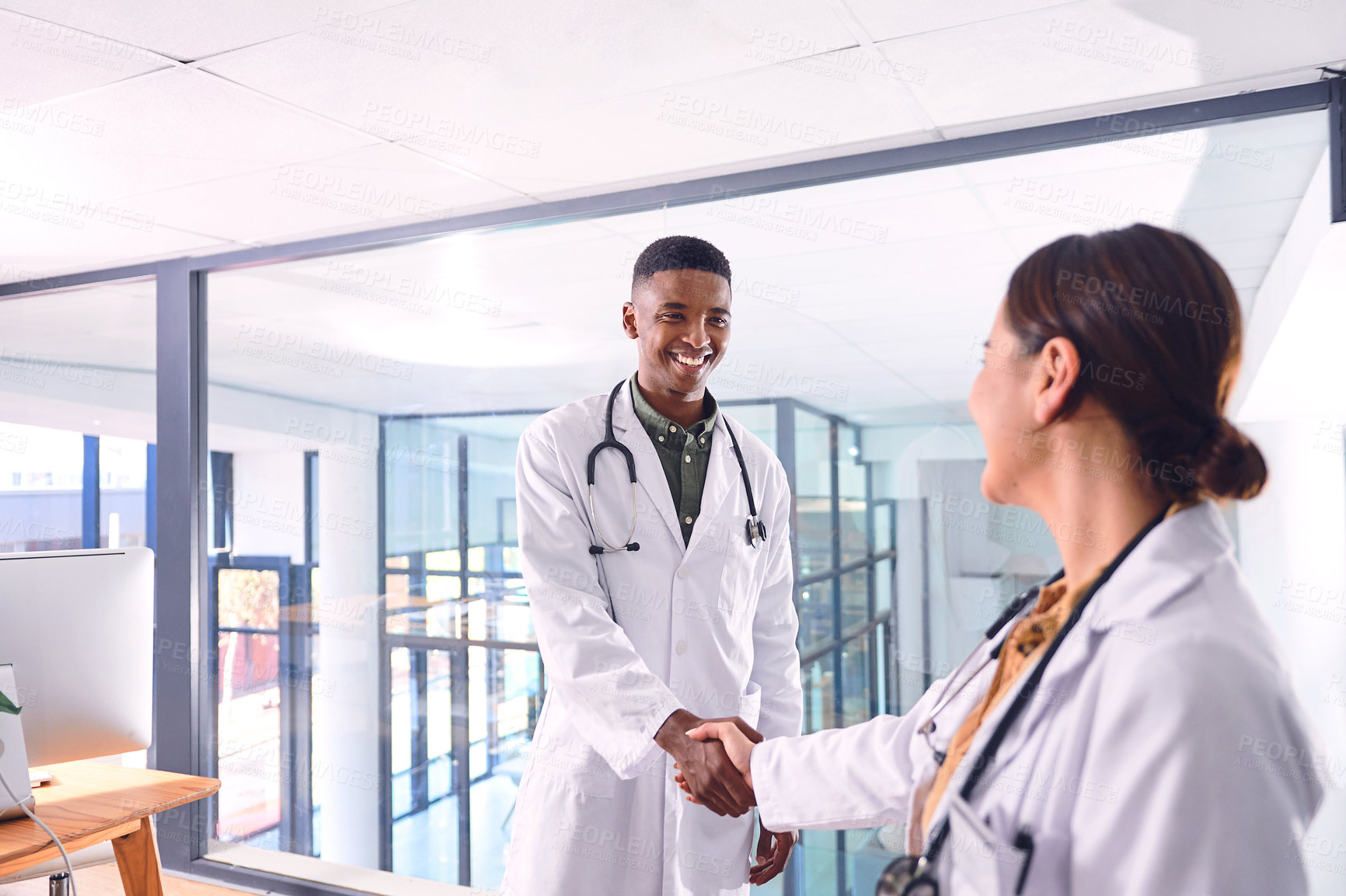 Buy stock photo Cropped shot of two young doctors shaking hands while standing in the hospital