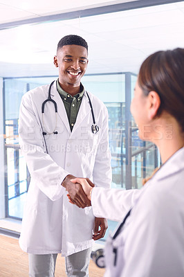 Buy stock photo Cropped shot of two young doctors shaking hands while standing in the hospital
