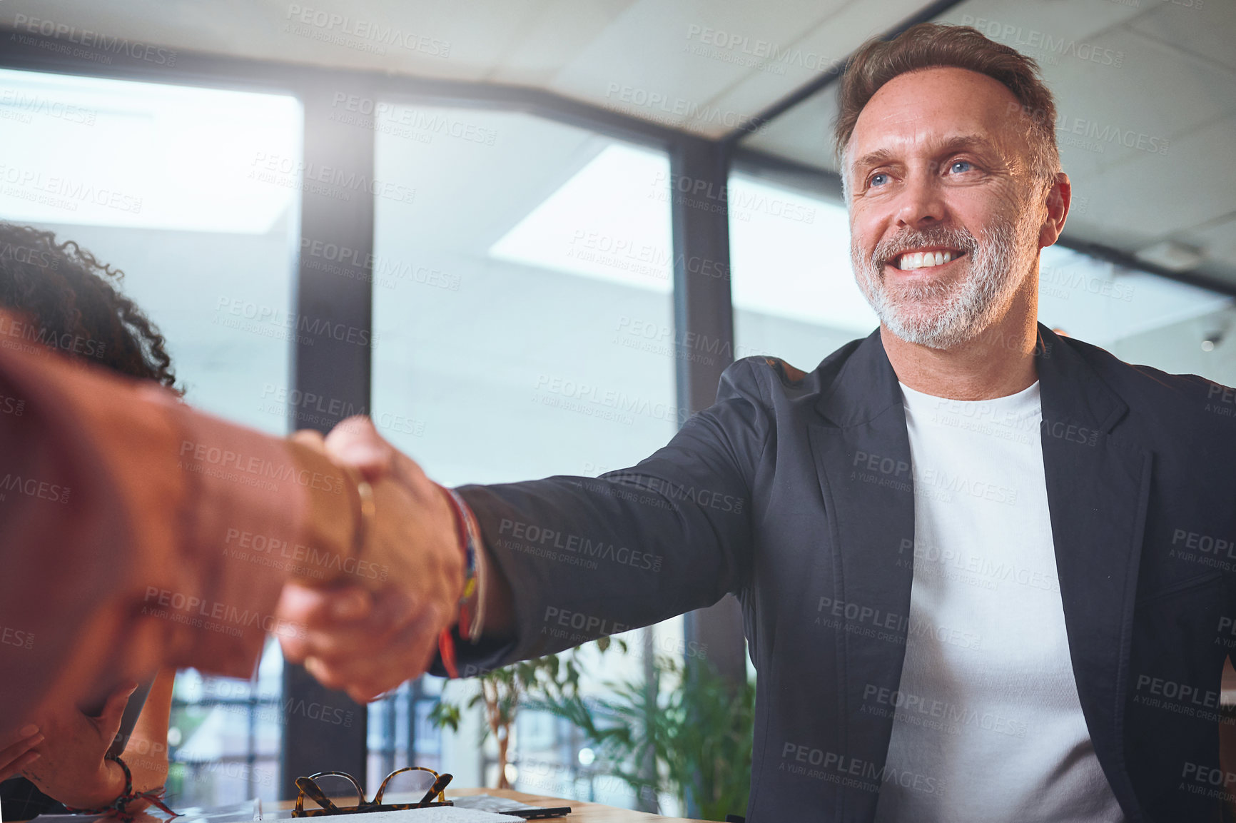 Buy stock photo Shot of a handsome mature businessman sitting and shaking a coworker's hand during a meeting in the office