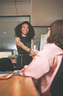 Buy stock photo Shot of two young businesswomen shaking hands during a meeting in the office