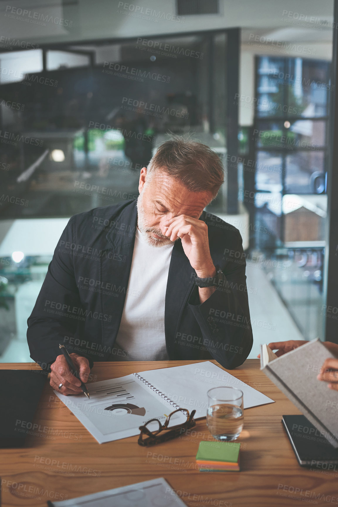 Buy stock photo Shot of a handsome mature businessman sitting alone in the office and feeling stressed while reading paperwork