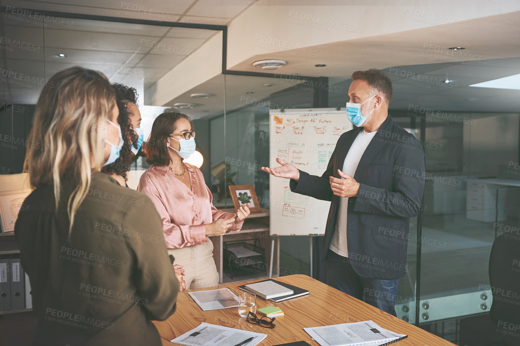 Buy stock photo Shot of a diverse group of businesspeople having a discussion during a meeting in the office while wearing face masks