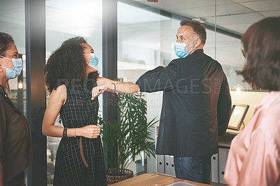 Buy stock photo Shot of two businesspeople standing together and elbowing each other while wearing face masks during a meeting in the office