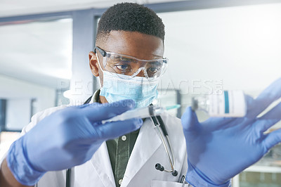Buy stock photo Shot of a young doctor extracting liquid with a syringe from a vial in an office