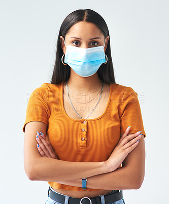 Buy stock photo Cropped shot of an attractive young woman standing with her arms folded while wearing a mask in studio against a grey background