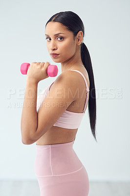 Buy stock photo Cropped portrait of an attractive young female athlete posing with a dumbbell in studio against a grey background