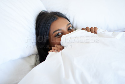 Buy stock photo High angle portrait of an attractive young woman peeking out from under the covers while lying in bed