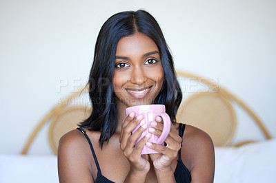 Buy stock photo Cropped portrait of an attractive young woman enjoying a cup of coffee while sitting on a bed