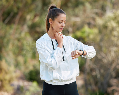 Buy stock photo Shot of a sporty young woman checking her pulse while exercising outdoors
