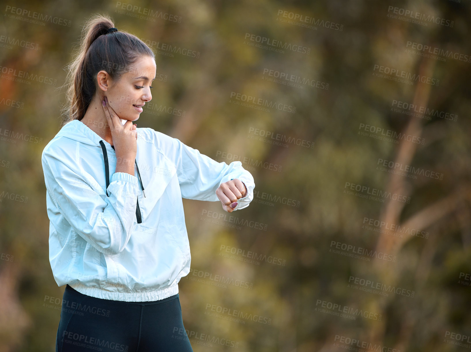 Buy stock photo Shot of a sporty young woman checking her pulse while exercising outdoors