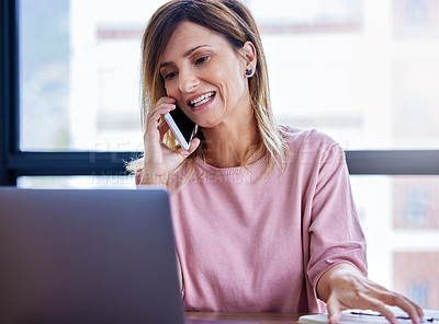 Buy stock photo Shot of a mature businesswoman talking on a cellphone while working on a laptop in an office
